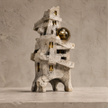 City of Silence brutalist tower sculpture with textured stone finish and gold sphere accent, front view on marble surface